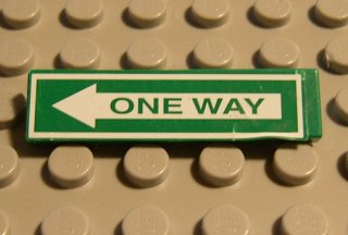 Green LEGO 1x4 tile with white 'ONE WAY' arrow pattern (sticker), pointing left, on a tan studded baseplate.