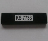 A black LEGO 1x4 tile with a white sticker featuring the text 'KS 7733' in black characters.