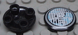 Two black LEGO 2654pb001 round 2x2 plates, one with bottom studs visible, the other with a white and blue headlight pattern.