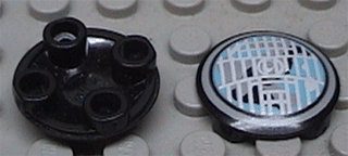 Two black LEGO 2654pb001 round 2x2 plates, one with bottom studs visible, the other with a white and blue headlight pattern.