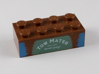 Brown LEGO 2x4 brick with 'TOW MATER' and 'Radiator Springs' printed on a sand green background with blue accents.