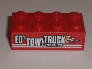 Red LEGO 2x4 brick with white 'ED'S TOW TRUCK & SERVICE' pattern and flame graphic on the side, from Set 8195.