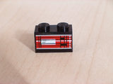 Black LEGO 1x2 brick 3004pb031R with a red and black taillight pattern, model right side, on a wooden surface.