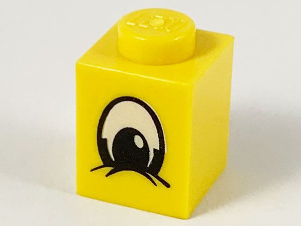 Yellow LEGO 1x1 brick, part 3005px2, with a black and white squinting eye print.