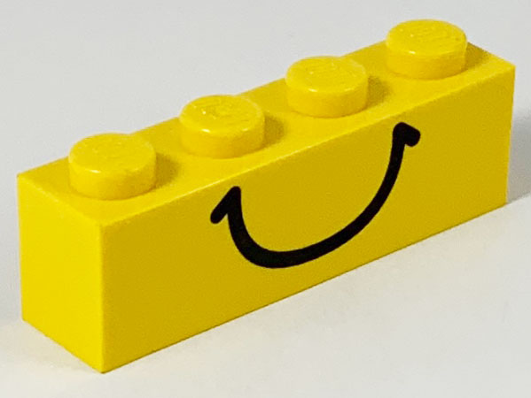 A bright yellow LEGO 1x4 brick with four studs on top and a black smiley face pattern printed on its side.