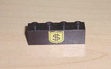 Close-up of a black LEGO 1x4 brick, model 3010pb017, with a yellow shield pattern featuring a dollar sign on a wooden surface.