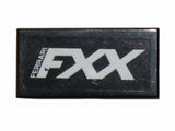 Close-up of a black LEGO 1x2 tile featuring a white 'FERRARI FXX' logo pattern, likely a sticker.