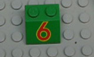 Green LEGO Slope 45 2x2 brick with a red number 6 outlined in yellow, resting on a grey LEGO baseplate.