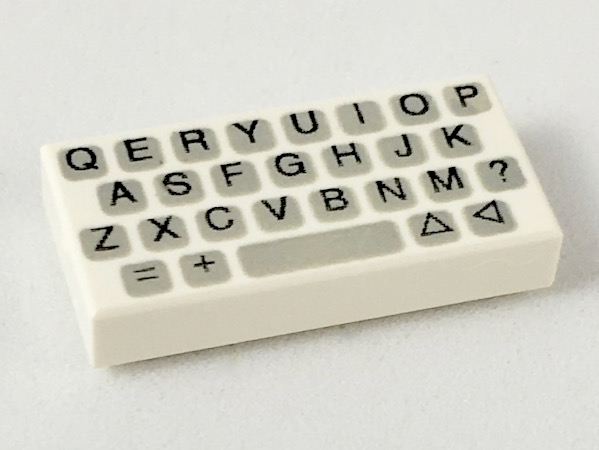 A white LEGO 1x2 tile featuring a black and grey printed pattern of a simplified QWERTY computer keyboard.