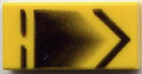 Yellow LEGO 1x2 tile with black chevron on the right, a broken line on the left, and a faded black pentagon pattern.