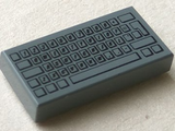 A dark gray LEGO 1x2 tile featuring a black print of a standard computer keyboard layout.