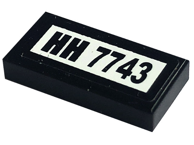 Black LEGO 1x2 tile, part 3069pb0108, with a white sticker featuring 'HH 7743' text, used in set 7743.