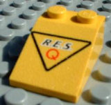 Yellow LEGO Slope 33 3x2 with 'R.E.S.' and red capital Q in black triangle pattern on a gray stud base.