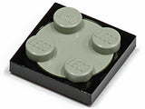 Close-up of a black LEGO 2x2 turntable plate with a light gray 2x2 rotating top piece that has four studs.