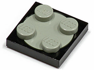 Close-up of a black LEGO 2x2 turntable plate with a light gray 2x2 rotating top piece that has four studs.