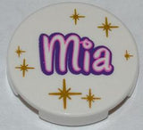Round white LEGO 2x2 tile with 'Mia' in purple and pink outline, surrounded by gold star patterns.