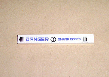 White LEGO 1x8 tile with a blue 'DANGER SHARP EDGES' sticker pattern, including exclamation mark and arrow symbols.