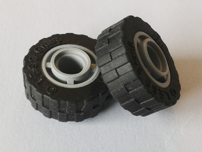 Two black LEGO tires with shallow staggered treads, mounted on grey 4-spoke wheel hubs.