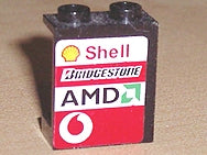 A black LEGO 1x2x2 panel with hollow studs, featuring a sticker with Shell, Bridgestone, AMD, and Vodafone logos.
