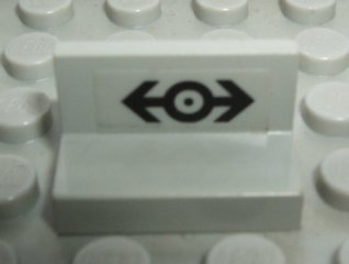White LEGO 4865pb021 Panel 1x2x1 with a black train logo pattern sticker featuring two arrows pointing away from a central circle.