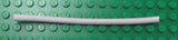 A white LEGO Pneumatic Hose (4mm D., 11L / 8.8cm) lying horizontally on a green LEGO baseplate with visible studs.