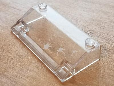 Clear LEGO Slope 33 3x6 part, 58181pb11, showing three bullet hole crack patterns, against a light brown wooden background.