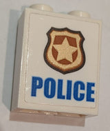 White LEGO 1x2x2 brick with inside stud holder, featuring blue 'POLICE' text and a gold and copper badge sticker.