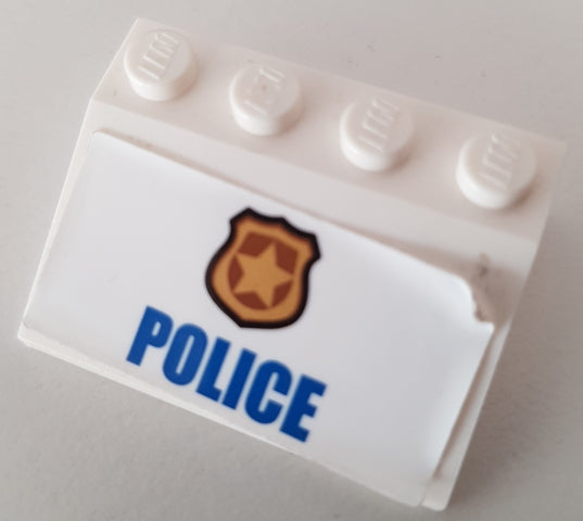 White LEGO Slope 33 3x4 brick with a sticker featuring a gold badge and blue 'POLICE' text. The sticker is slightly peeling.