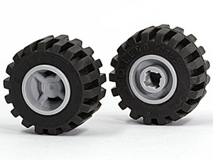 Two black LEGO tires with offset wide tread on light gray hubs. One wheel shows the outer hub, the other the notched pin hole.