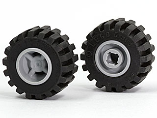Two black LEGO tires with offset wide tread on light gray hubs. One wheel shows the outer hub, the other the notched pin hole.