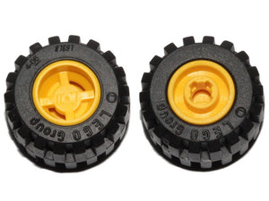 Two black LEGO wheels (87697) with yellow hubs, offset tread tires, and notched holes for wheel holder pins, against a white background.