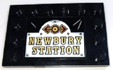 Black LEGO 4x6 tile with studs on edges, featuring a sticker with a dark red and gold train logo above 'NEWBURY STATION' text.