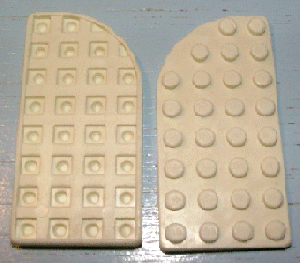 Two off-white LEGO 713old Plate, Round Curved 4 x 8 Right pieces. One shows the waffle bottom, the other the studded top.