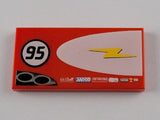 Red LEGO 2x4 tile with '95' in a black circle, a yellow lightning bolt on a white half-ellipse, and small sponsor logos.