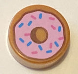 Round 1x1 LEGO tile with a doughnut pattern, featuring pink frosting and blue and pink sprinkles.