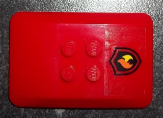 Red LEGO 6x4x2/3 wedge with four visible studs and a transparent sticker featuring a black and yellow fire logo badge.