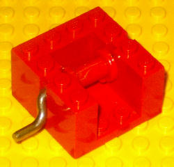 Red LEGO bb0067 String Reel Winch 4x4x2 with a curved silver metal handle, on a yellow LEGO studded background.