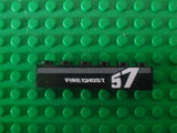 Close-up of a black LEGO 1x6 brick with a white and gray 'FIRE GHOST' and '57' pattern on a green baseplate.