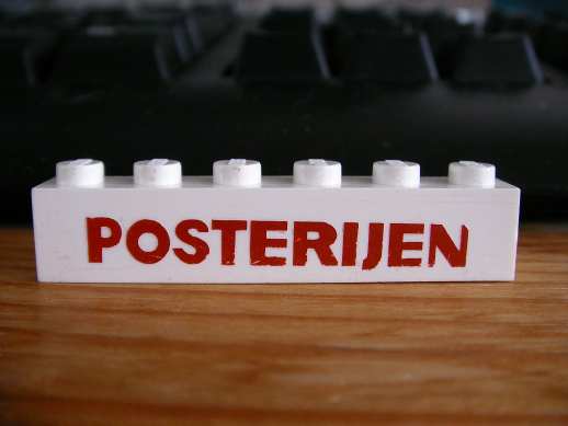 White LEGO 1x6 brick with red text 'POSTERIJEN' in bold font, on a wooden surface with a keyboard in background.