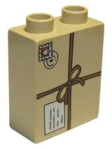 A tan LEGO Duplo 1x2x2 brick featuring a tied parcel pattern with a postmark displaying a face and a message tag.