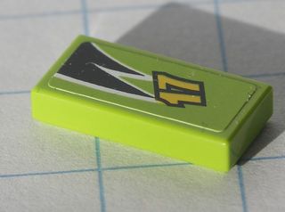 Close-up of a lime green LEGO 1x2 tile with a yellow '17' and black and white flame pattern on top.