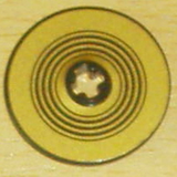Close-up of a gold LEGO Technic Disk 3x3 with concentric black rings pattern and a central hole.
