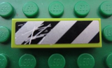 Lime green LEGO 1x3 tile with scratched black and silver/white danger stripe sticker, on a green LEGO baseplate.