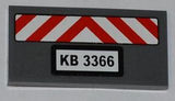 Dark gray LEGO 2x4 tile with red and white chevron danger stripes and a 'KB 3366' license plate sticker.