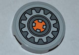 Light gray LEGO Tile, Round 2x2, featuring a dark bluish gray gear wheel pattern with an orange square center.