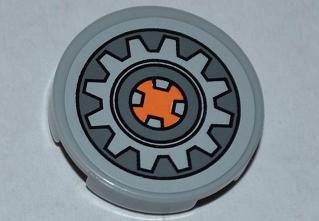 Light gray LEGO Tile, Round 2x2, featuring a dark bluish gray gear wheel pattern with an orange square center.